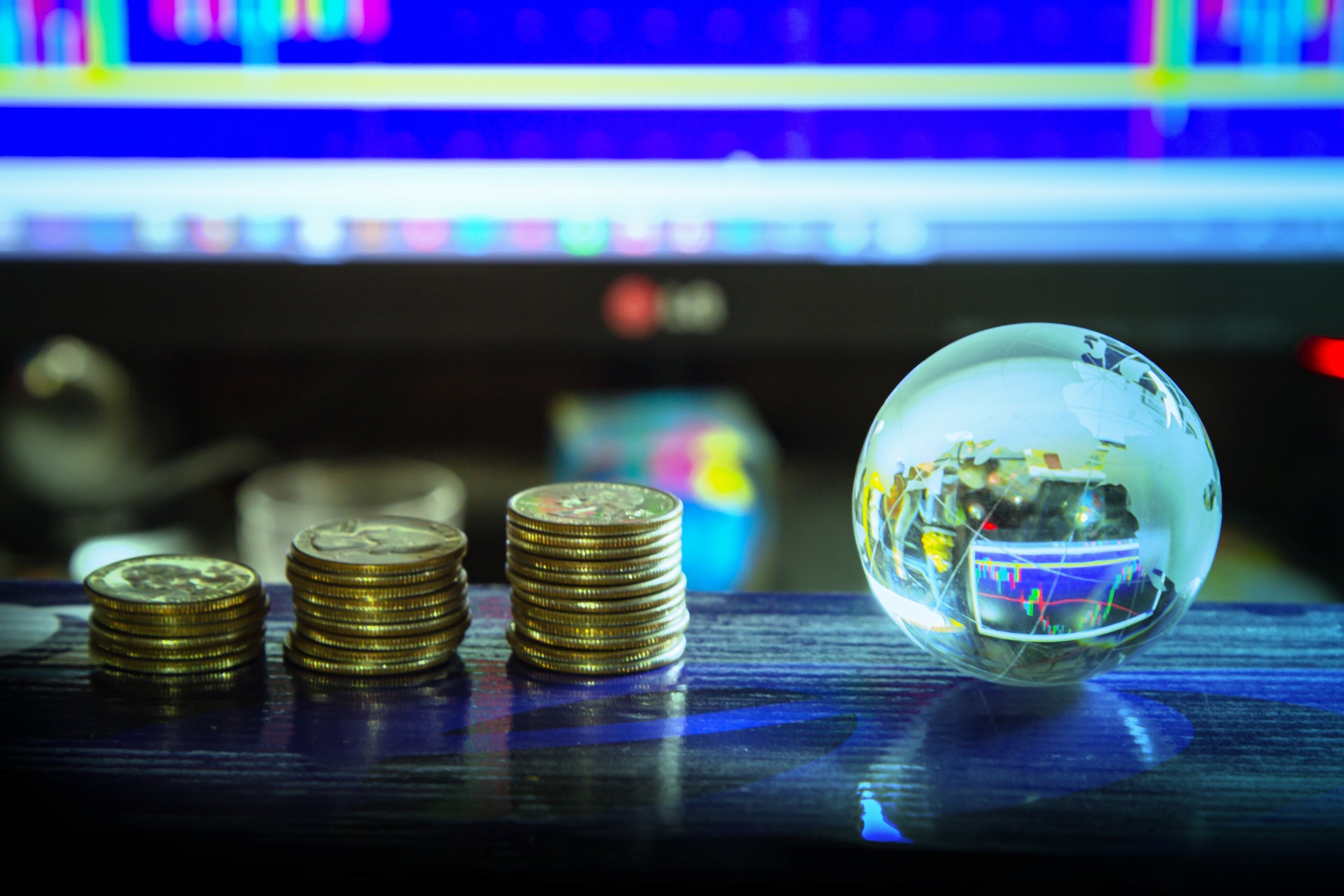 Arrangement of World globe crystal glass and coin at office table on charts stock data on computer screen background. Global business on financial concept. World wide technology.